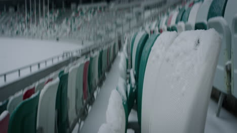 Empty-outdoor-football-soccer-stadium-seats-covered-with-snow-in-winter,-light-snowfall.-Shot-with-2x-anamorphic-lens.-120-FPS-Slow-motion